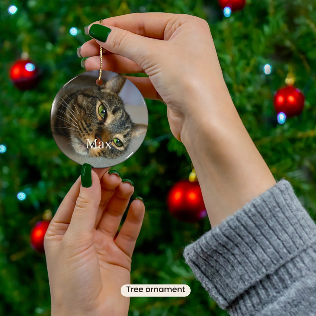 The Portrait Ornament with a cat's photo and name, held up to a Christmas tree